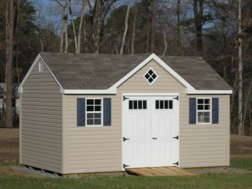 tan a frame dormer shed with white doors in front of trees
