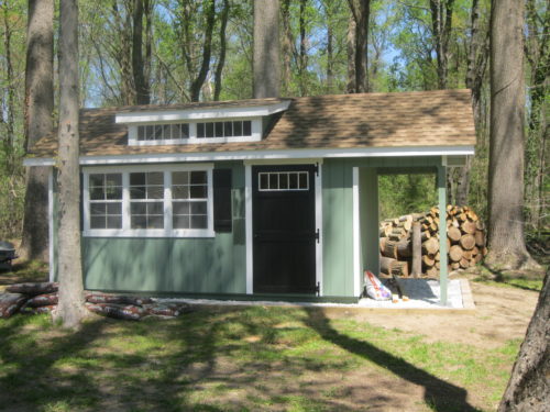 green classic studio dormer shed with pile of wood in back