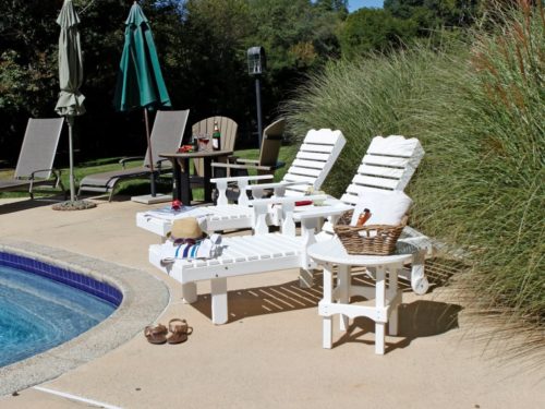 white outdoor lawn furniture sitting between pool and outdoor foliage